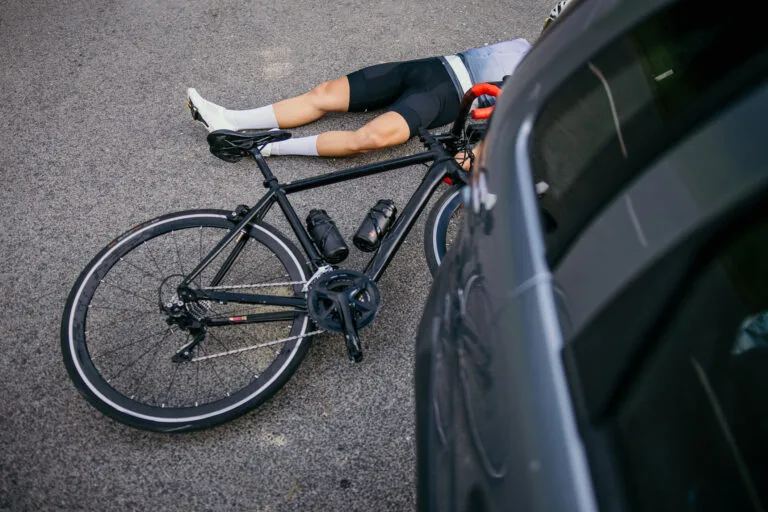 Cyclist lying on the road next to the car.